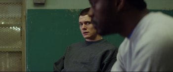 Movie still from “Starred Up” (2013), directed by David Mackenzie – A man looking at the camera while standing next to another man; Medium shot, Over the shoulder angle