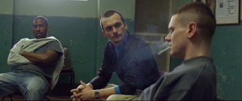 Movie still from “Starred Up” (2013), directed by David Mackenzie – A man sitting next to another man smoking a cigarette; Medium shot, Over the shoulder angle