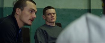 Movie still from “Starred Up” (2013), directed by David Mackenzie – A man in a gray sweatshirt is looking into the camera; Medium shot, Over the shoulder angle