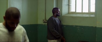 Movie still from “Starred Up” (2013), directed by David Mackenzie – A man standing next to a window in a room; Medium shot, Over the shoulder angle
