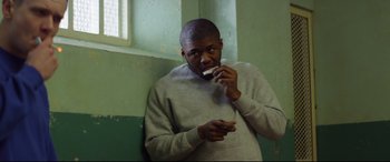 Movie still from “Starred Up” (2013), directed by David Mackenzie – A man eating something while standing in a room; Medium shot, Over the shoulder angle