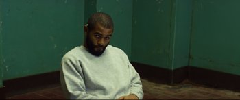 Movie still from “Starred Up” (2013), directed by David Mackenzie – A man sitting in front of a green wall; Medium shot, Over the shoulder angle