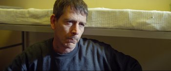 Movie still from “Starred Up” (2013), directed by David Mackenzie – A person sitting on a couch; Close Up shot, Over the shoulder angle