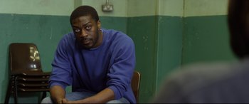 Movie still from “Starred Up” (2013), directed by David Mackenzie – A man sitting at a table in front of a green wall; Medium shot, Over the shoulder angle
