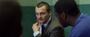 Movie still from “Starred Up” (2013), directed by David Mackenzie – A person wearing a suit and tie; Close Up shot, Over the shoulder angle