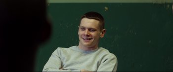 Movie still from “Starred Up” (2013), directed by David Mackenzie – A young man sitting in front of a green wall; Medium shot, Over the shoulder angle