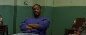 Movie still from “Starred Up” (2013), directed by David Mackenzie – A man with his arms crossed sitting in a room; Medium shot, Over the shoulder angle