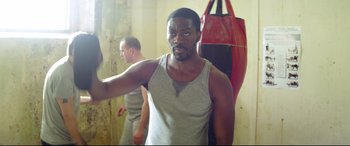 Movie still from “Starred Up” (2013), directed by David Mackenzie – A man standing in front of a punching bag in a room; Medium shot, Over the shoulder angle