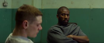 Movie still from “Starred Up” (2013), directed by David Mackenzie – Two men sitting in a room , one of whom is wearing a blanket and the other is wearing a sweatshirt; Medium shot, Over the shoulder angle