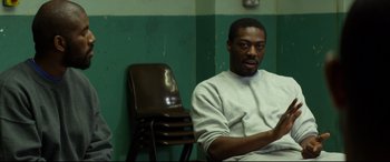 Movie still from “Starred Up” (2013), directed by David Mackenzie – A man sitting in a room next to a brown chair; Medium shot, High angle