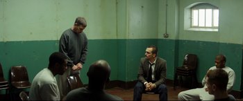 Movie still from “Starred Up” (2013), directed by David Mackenzie – A group of men sitting on the ground in front of a green wall; Wide shot, Over the shoulder angle