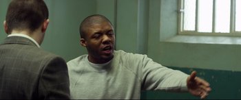 Movie still from “Starred Up” (2013), directed by David Mackenzie – A man sitting in front of a window with his mouth open; Medium shot, Low angle