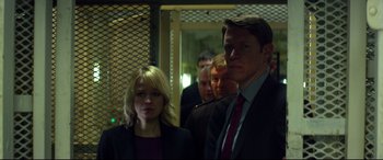 Movie still from “Starred Up” (2013), directed by David Mackenzie – A man and a woman standing next to each other in front of other men; Medium shot, Low angle