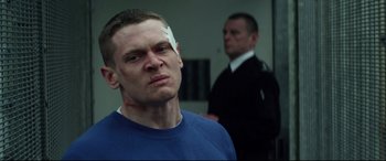 Movie still from “Starred Up” (2013), directed by David Mackenzie – A man with bandages on his head and a police officer standing behind him; Close Up shot, Over the shoulder angle