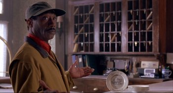 Movie still from “State and Main” (2000), directed by David Mamet – A man standing in front of a table with a plate on top of it; Medium shot, Low angle