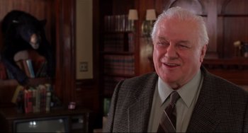 Movie still from “State and Main” (2000), directed by David Mamet – An older man wearing a suit and tie in front of a bookcase; Close Up shot, Low angle