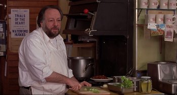 Movie still from “State and Main” (2000), directed by David Mamet – A man sitting at a table in front of a stove; Close Up shot, Low angle