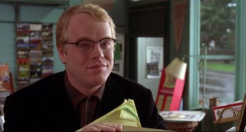 Movie still from “State and Main” (2000), directed by David Mamet – A man sitting at a table holding a piece of paper; Close Up shot, Over the shoulder angle