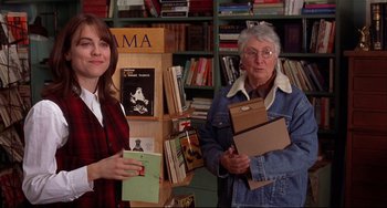 Movie still from “State and Main” (2000), directed by David Mamet – Two women standing next to each other in front of a bookcase; Medium shot, Over the shoulder angle
