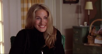 Movie still from “State and Main” (2000), directed by David Mamet – A woman smiling for the camera while sitting in a chair; Close Up shot, Over the shoulder angle