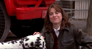 Movie still from “State and Main” (2000), directed by David Mamet – A woman holding a dalmatian dog in front of a red truck; Close Up shot, Over the shoulder angle