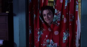Movie still from “State and Main” (2000), directed by David Mamet – A woman peeks out from behind a red curtain; Medium shot, Low angle