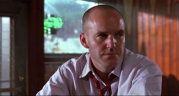 Movie still from “State and Main” (2000), directed by David Mamet – A bald man with a red tie sitting in front of a tv; Close Up shot, Low angle
