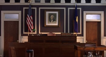 Movie still from “State and Main” (2000), directed by David Mamet – A judge's bench in front of a portrait of george washington; Wide shot, Low angle