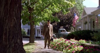 Movie still from “State and Main” (2000), directed by David Mamet – A man walking down a sidewalk near a tree and flowers; Wide shot, Low angle
