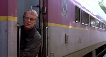Movie still from “State and Main” (2000), directed by David Mamet – A man sitting on the side of a purple train; Medium shot, Over the shoulder angle