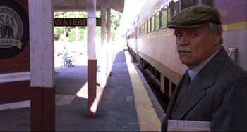 Movie still from “State and Main” (2000), directed by David Mamet – An older man standing in front of a train station; Medium shot, Over the shoulder angle