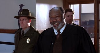 Movie still from “State and Main” (2000), directed by David Mamet – A man in a suit and tie standing next to another man in a suit and tie; Medium shot, Low angle