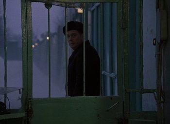 Movie still from “A Railway Station for Two” (1983), directed by Eldar Ryazanov – A man standing behind bars in front of a fence; Medium shot, Over the shoulder angle