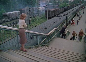 Movie still from “A Railway Station for Two” (1983), directed by Eldar Ryazanov – A woman standing on a set of stairs next to train tracks; Wide shot, High angle