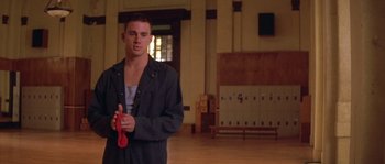 Movie still from “Step Up” (2006), directed by Anne Fletcher – A young man holding a pair of shoes in a room; Medium shot, Low angle
