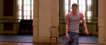 Movie still from “Step Up” (2006), directed by Anne Fletcher – A man standing next to a chair in a room; Wide shot, Low angle