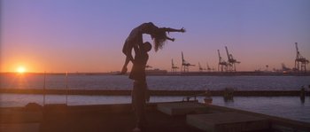 Movie still from “Step Up” (2006), directed by Anne Fletcher – A man and a woman are doing acrobatics in front of a body of water; Wide shot, Low angle