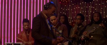 Movie still from “Step Up” (2006), directed by Anne Fletcher – A group of people in a room with a microphone; Medium shot, Over the shoulder angle