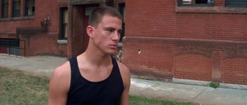 Movie still from “Step Up” (2006), directed by Anne Fletcher – A man in a black tank top is standing in front of a brick building; Close Up shot, High angle