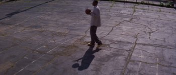 Movie still from “Step Up” (2006), directed by Anne Fletcher – A man is walking in a parking lot holding a basketball; Extreme Wide shot, High angle