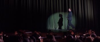 Movie still from “Step Up” (2006), directed by Anne Fletcher – A man standing in front of a curtain on a stage; Wide shot, Low angle