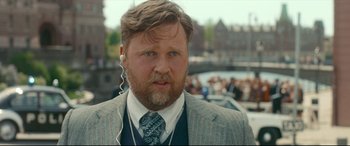Movie still from “Stockholm” (2018), directed by Robert Budreau – A man in a suit and tie with headphones; Close Up shot, Over the shoulder angle