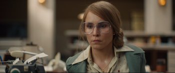 Movie still from “Stockholm” (2018), directed by Robert Budreau – A woman wearing glasses and a green jacket looking at the camera; Close Up shot, Over the shoulder angle