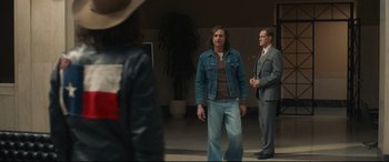 Movie still from “Stockholm” (2018), directed by Robert Budreau – A man wearing a jean jacket standing next to another man wearing a suit; Medium shot, Over the shoulder angle