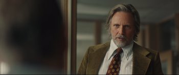 Movie still from “Stockholm” (2018), directed by Robert Budreau – An older man with long grey hair wearing a suit and tie; Close Up shot, Over the shoulder angle