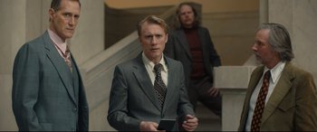 Movie still from “Stockholm” (2018), directed by Robert Budreau – A man in a suit and tie standing next to another man in a suit and tie; Medium shot, Low angle