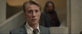 Movie still from “Stockholm” (2018), directed by Robert Budreau – A person wearing a suit and tie; Close Up shot, Over the shoulder angle