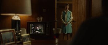 Movie still from “Stockholm” (2018), directed by Robert Budreau – A man standing in front of a tv in a room; Medium shot, Over the shoulder angle