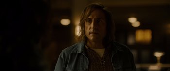 Movie still from “Stockholm” (2018), directed by Robert Budreau – A man with long brown hair wearing a jean jacket; Close Up shot, Over the shoulder angle