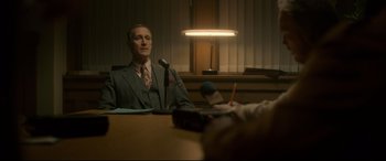 Movie still from “Stockholm” (2018), directed by Robert Budreau – A man sitting at a table in front of a microphone; Medium shot, Over the shoulder angle